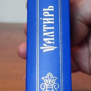 May include: A blue book spine with ornate silver-colored designs and text. The text reads "Уалтирь" in Cyrillic script. A blue bookmark is attached.