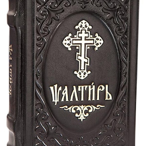 May include: A black book with an embossed cross and ornate detailing. The cover features the word "Psalter" in gold lettering. The book has a textured appearance and a decorative border around the cross.
