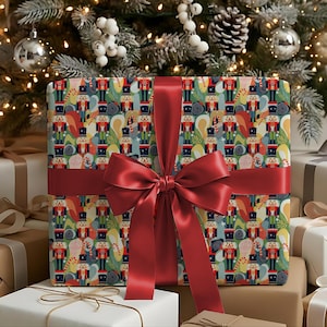 Könnte beinhalten: Eine quadratische Geschenkbox, eingewickelt in Papier mit einem wiederkehrenden Muster aus bunten Nussknackern, Zuckerstangen und Blattwerk. Die Box ist mit einem breiten, glatten, dunkelroten Satinband umwickelt, das vorne zu einer großen Schleife gebunden ist.
