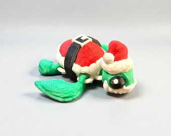 May include: A whimsical Christmas-themed turtle figurine. The turtle's shell is designed to resemble Santa's suit, with a red top and a black belt. The turtle's head wears a Santa hat, and its body is green.