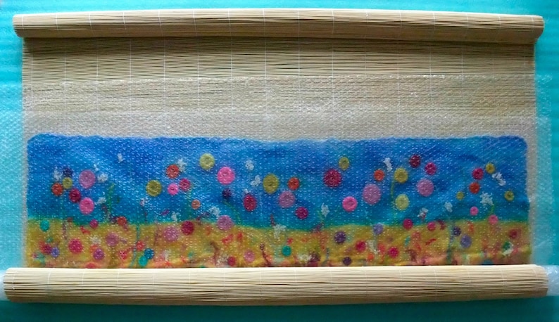 A process image from the PDF tutorial showing the felt being rolled in a rolling mat.  The mat is only half rolled up to show the work inside the mat