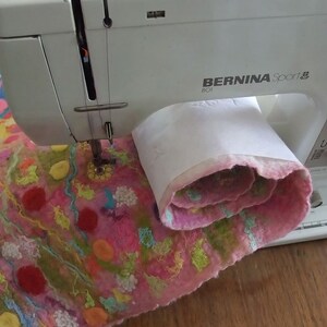 An image from the PDF tutorial showing the felted artwork being stitched on a Bernina sewing machine.  The felted artwork is partly rolled up to demonstrate how to sew a big piece on a small machine bed