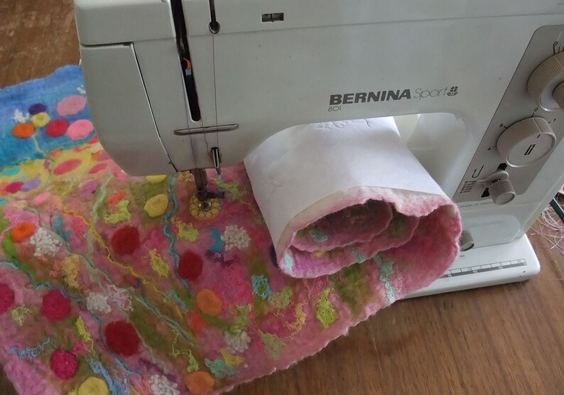 An image from the PDF tutorial showing the felted artwork being stitched on a Bernina sewing machine.  The felted artwork is partly rolled up to demonstrate how to sew a big piece on a small machine bed