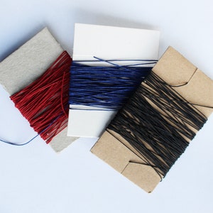May include: Three spools of thread in red, blue, and black. The thread is wound around cardboard spools. The spools are arranged diagonally on a white surface. The thread appears to be a fine, smooth material.
