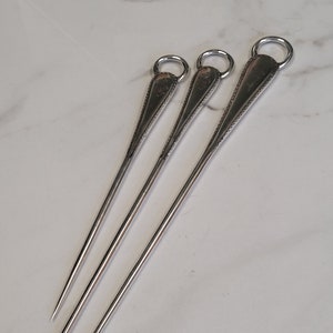 Könnte beinhalten: Drei silberne Spieße mit Schlaufe. Die Spieße sind unterschiedlich lang.