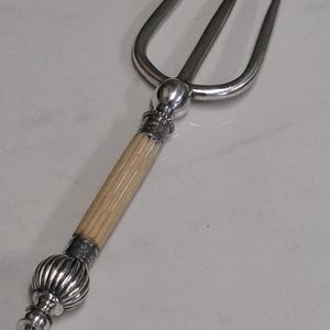 May include: A silver and ivory handled fish fork with three prongs. The fork has a decorative ball finial at the end of the handle.