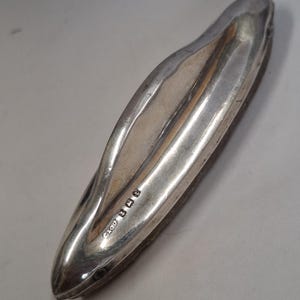 May include: Silver nail buffer with a curved design and the inscription "Glou 1918" on the side.