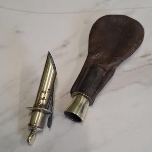 Peut inclure: Une ancienne flasque à poudre en argent et en cuir, avec un embout en argent et une pochette en cuir marron. La flasque est conçue pour contenir de la poudre à canon ou d'autres poudres fines. L'embout est détaché de la pochette.