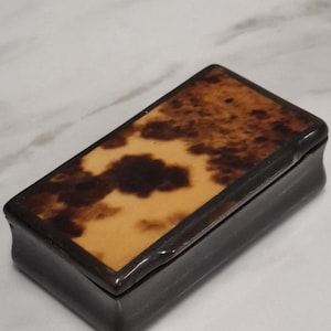 以下が含まれることがあります： 長方形の箱で、蓋にはべっ甲模様があります。蓋は光沢のある仕上がりで、濃い茶色とタンの色合いです。箱自体は濃い茶色です。