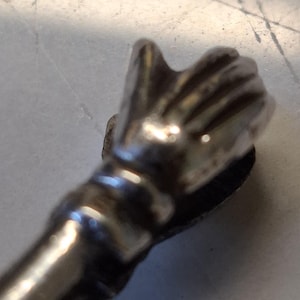 Op de afbeelding: Een zilverkleurige flesstopper met een handontwerp. De hand is gebeeldhouwd met gedetailleerde vingers en een licht open handpalm, bevestigd aan een cilindrische steel. De stopper is waarschijnlijk voor een wijn- of likeurfles.