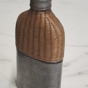 Könnte beinhalten: Eine weiße Keramik-Tasse mit schwarzem Henkel und dem Text "But First, Coffee" in fetter, schwarzer Schrift. Die Tasse steht vor einem verschwommenen Hintergrund, der eine gemütliche Umgebung suggeriert.