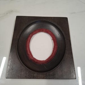 May include: A dark brown, square wooden tray with a circular indentation. Inside the indentation is a red, textured ring surrounding a white centre. The tray is likely for decorative or functional use.