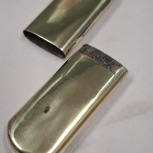 Peut inclure: Un étui à cigarettes rectangulaire de couleur or avec un couvercle séparé. L'étui est ouvert, révélant l'intérieur. L'étui a des bords arrondis et une surface lisse et polie. Le couvercle est également doré et de forme similaire.