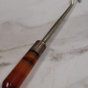 Peut inclure: Un chausse-pied en argent avec une poignée en plastique brun et orange. La poignée est en plastique marbré.