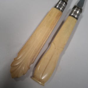 May include: Two antique silver-plated butter knives with ivory handles. The handles are carved with a floral design.