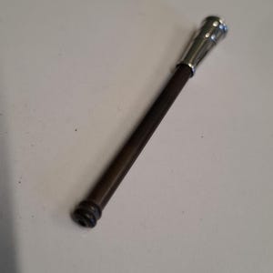 May include: A brown and silver smoking pipe. The pipe has a silver mouthpiece and a long, slender stem. The bowl is small. The pipe is made of metal and wood.