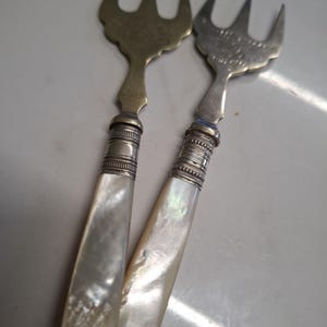 May include: Two antique silver forks with mother of pearl handles. The forks have ornate designs and are in excellent condition.