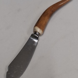 Puede incluir: Un cuchillo de mantequilla de acero inoxidable con un mango de asta de ciervo marrón. El mango tiene una punta blanca.