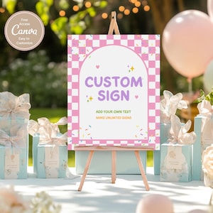 May include: A custom sign on a wooden easel with a pink and white checkered border. The sign reads "CUSTOM SIGN" in purple text, with the option to add your own text. The background includes gift boxes, balloons, and floral arrangements.