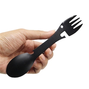 May include: Black multi-tool utensil with a spoon, fork, bottle opener, and serrated edge. The utensil is held in a hand against a white background. This camping and outdoor tool is made of metal.