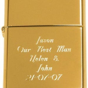 May include: A gold-coloured lighter with engraved text. The text reads "Jason, Our Best Man, Helen & John, 21-07-07". The lighter has a rectangular shape with rounded edges and a hinged lid.