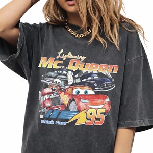 Puede incluir: Camiseta gris oscuro con un dise&ntilde;o de Rayo McQueen y otros personajes de la pel&iacute;cula Cars. El dise&ntilde;o incluye el texto "Lightning Mc. Queen", "95" y "think fast".