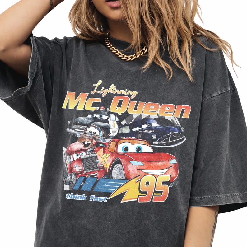 Puede incluir: Camiseta gris oscuro con un dise&ntilde;o de Rayo McQueen y otros personajes de la pel&iacute;cula Cars. El dise&ntilde;o incluye el texto "Lightning Mc. Queen", "95" y "think fast".