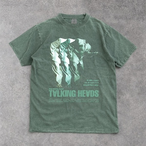 May include: Green short-sleeve t-shirt featuring a graphic of three figures in suits. The text "TVLKING HEVDS" is printed in a green font at the bottom of the shirt, with additional text above and to the right of the graphic.