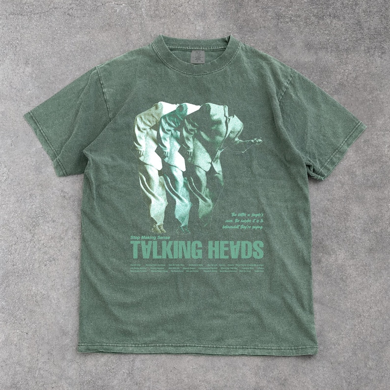 May include: Green short-sleeve t-shirt featuring a graphic of three figures in suits. The text "TVLKING HEVDS" is printed in a green font at the bottom of the shirt, with additional text above and to the right of the graphic.