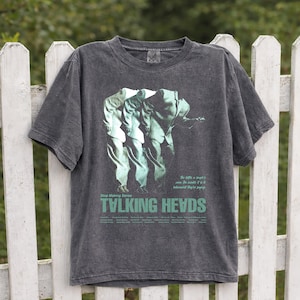 Puede incluir: Camiseta gris oscuro con un gráfico verde de tres figuras con trajes y el texto "Stop Making Sense" encima de "TALKING HEADS" en verde. La camiseta tiene un aspecto vintage.