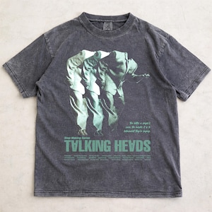 May include: Dark gray t-shirt featuring a graphic of three figures in suits with a green overlay. The text "Stop Making Sense" and "TALKING HEADS" is printed in green. The shirt has a vintage, washed look.