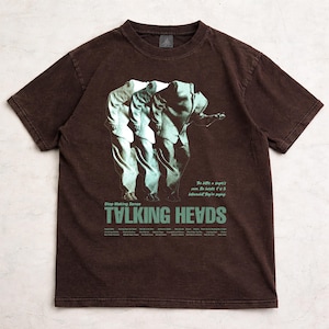 May include: Brown t-shirt featuring a graphic of three figures in suits, with the words "TALKING HEADS" in green. The shirt also includes the text "Stop Making Sense" and other text below the band's name.