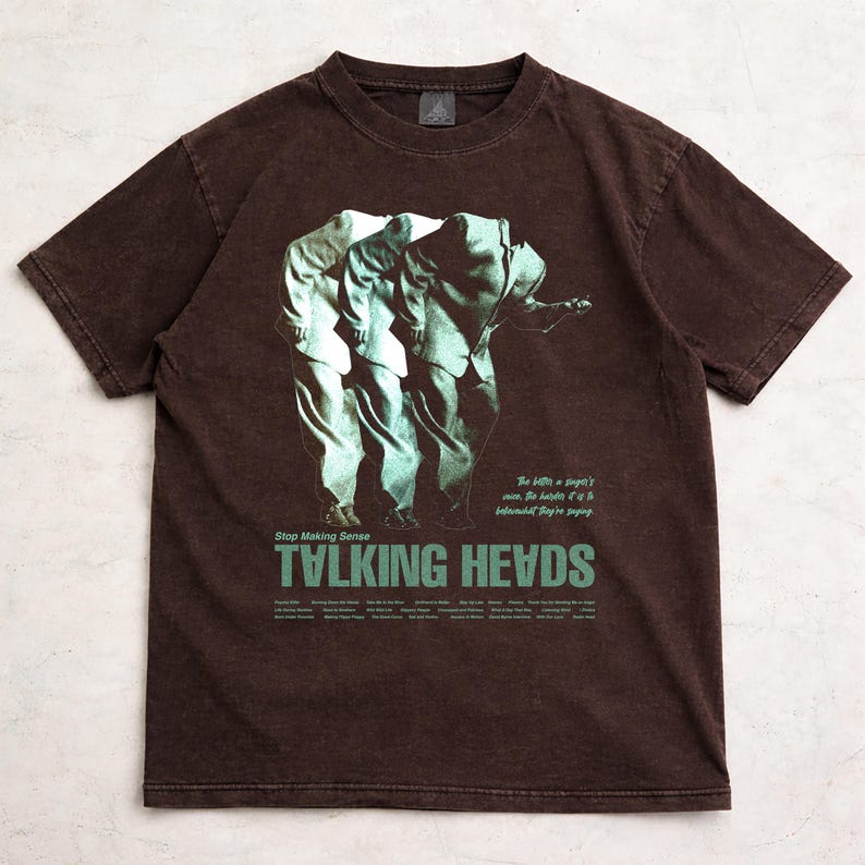 May include: Brown t-shirt featuring a graphic of three figures in suits, with the words "TALKING HEADS" in green. The shirt also includes the text "Stop Making Sense" and other text below the band's name.