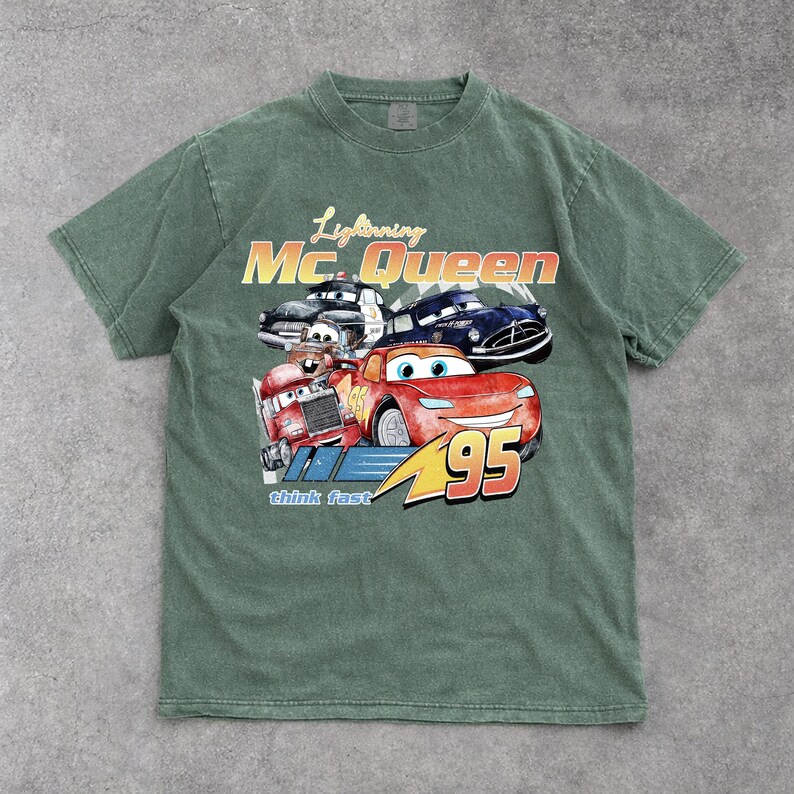 Puede incluir: Camiseta verde con un dise&ntilde;o de Rayo McQueen y otros personajes de Cars. El dise&ntilde;o incluye el texto "Lightning Mc. Queen" y "95". La camiseta tiene un aspecto vintage y desgastado.
