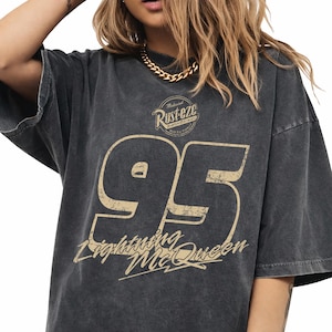 May include: Charcoal grey Lightning McQueen t-shirt featuring the number 95 in tan. The shirt also displays the text "Rust-eze Bumper Ointment" and "Lightning McQueen" in a vintage style.
