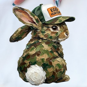 May include: A white sweatshirt featuring a detailed illustration of a camouflage-patterned bunny wearing a green and white cap with the text "EGG HUNTER". The bunny has a fluffy white tail and brown eyes.