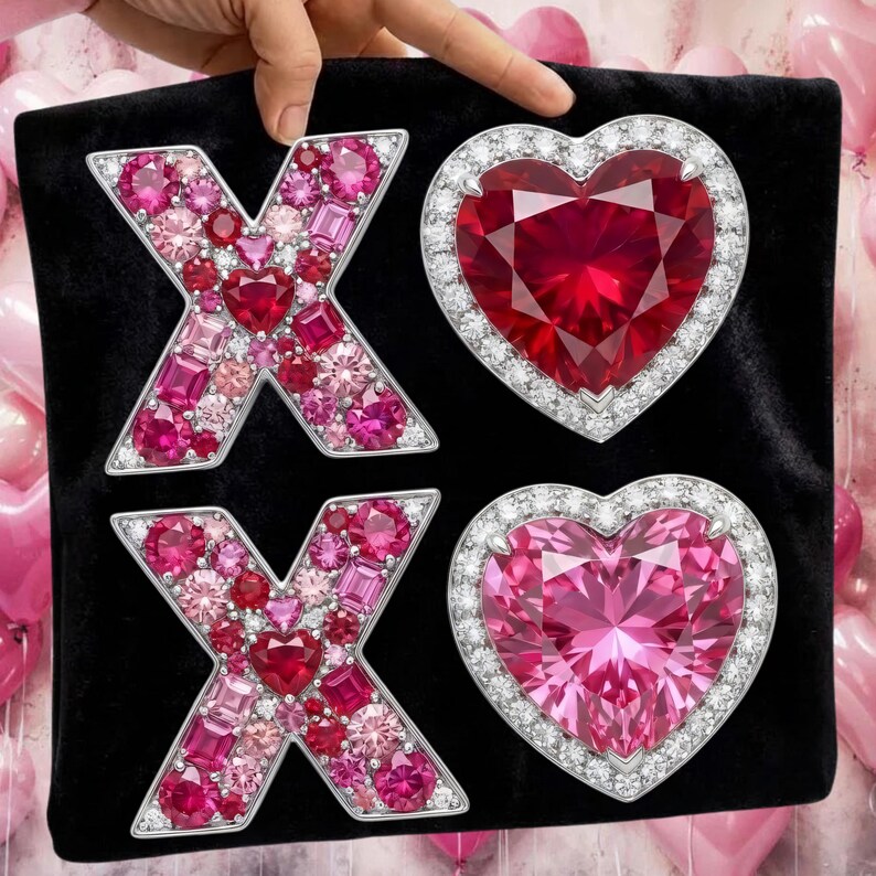 Puede incluir: Una superficie de terciopelo negro muestra dos formas de 'X' y dos formas de coraz&oacute;n, todas adornadas con piedras preciosas rosas y rojas. Las piedras est&aacute;n engastadas en un metal plateado, creando un efecto brillante. Globos rosas en el fondo.