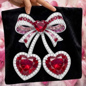 Puede incluir: Broche con forma de lazo y dos corazones. El broche presenta un gran rub&iacute; en forma de coraz&oacute;n en el centro del lazo y dos colgantes de coraz&oacute;n de rub&iacute;. El broche est&aacute; incrustado con piedras preciosas blancas y rosas y engastado en metal plateado.