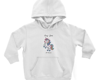 May include: White hooded sweatshirt featuring a colorful unicorn graphic with the text "Lucy-Jane" and "Lil Unicorn". The unicorn has a rainbow mane and tail, and is standing on its hind legs. The sweatshirt has a kangaroo pocket.
