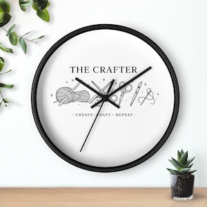 Puede incluir: Un reloj de pared redondo con marco negro y esfera blanca. La esfera del reloj presenta el texto "THE CRAFTER" sobre ilustraciones de herramientas de artesanía. Debajo, la frase "- CREATE - CRAFT - REPEAT -."
