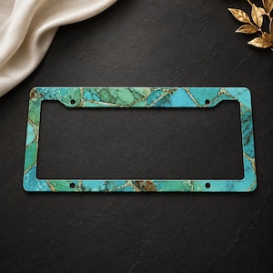 May include: A rectangular license plate frame featuring a vibrant turquoise and teal stone pattern with intricate gold veining throughout. The frame has four circular mounting holes positioned at the corners to secure it to a vehicle's license plate.