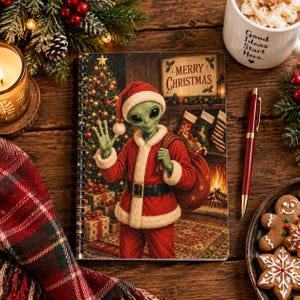 May include: A spiral-bound notebook featuring a green alien dressed in a red and white Santa Claus suit, waving a hand, with a Christmas tree, gifts, and a sign that reads Merry Christmas in the background, set against a festive holiday scene.