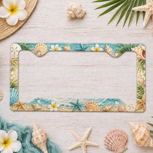 May include: A rectangular license plate frame featuring a beach-themed design with a sandy shoreline, turquoise ocean waves, white plumeria flowers, various seashells, starfish, and green palm leaves printed across the entire surface.