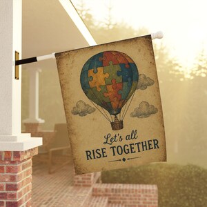 May include: A rectangular flag with a vintage design. The flag features a hot air balloon composed of puzzle pieces in various colours. The text "Let's all RISE TOGETHER" is printed below the balloon. The flag is mounted on a white pole.