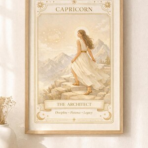 May include: Framed art print featuring a woman in a flowing white dress ascending stone steps, with mountains in the background. The print is labeled "CAPRICORN" and "THE ARCHITECT," with the words "Discipline, Patience, Legacy" below. The artwork has a warm, neutral color palette.
