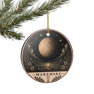 May include: A round ceramic ornament featuring a dark celestial scene with a large textured moon, starry sky, and a rocky landscape. The design includes floral accents and the text MAKEMAKE with a symbol below, suspended by a gold string.