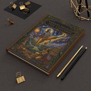 May include: A rectangular notebook with a dark brown cover featuring a detailed illustration of Vamana measuring the universe, with the text VAMANA MEASURES THE UNIVERSE printed in gold. The cover includes gold accents, peacock feathers, and lotus motifs.