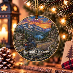 Op de afbeelding: Een rond keramisch ornament met een motorrijder op de Beartooth Highway. De afbeelding toont bergen, een meer en een bord met de tekst Elevation 10,947 FT. De tekst bevat Beartooth Highway, Montana / Wyoming en Ride Explore Adventure.