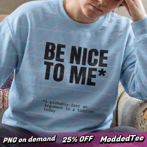 以下が含まれることがあります： 「BE NICE TO ME*」の黒い文字がプリントされた水色のスウェットシャツ。下には「*i probably lost an argument to a toddler today」と書かれています。クルーネックのデザインです。