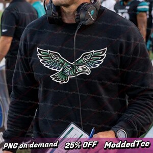 Può includere: Felpa nera con un design stilizzato di un'aquila verde e bianca. La grafica dell'aquila è centrata sul petto. L'immagine include anche il testo in basso che recita "PNG on demand 25% OFF ModdedTee".